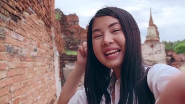 クローズアップ若いアジアのバックパッカーブロガーの女性カジュアルルックカメラのビデオ通話スマートフォンのライブオンラインで観客の旅行のために一緒にパゴダ旧市街で ライフスタイル観光旅行休日のコンセプト — ストック動画
