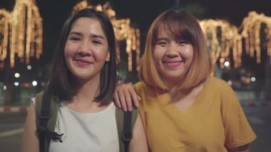 Mutlu Asyalı genç kızlar, sıradan bir şekilde gülümseyen turistlerle şehir sokaklarındaki arka plandaki barışçıl fotoğraflara bakıyorlar. Yaşam tarzı turist seyahati konsepti.