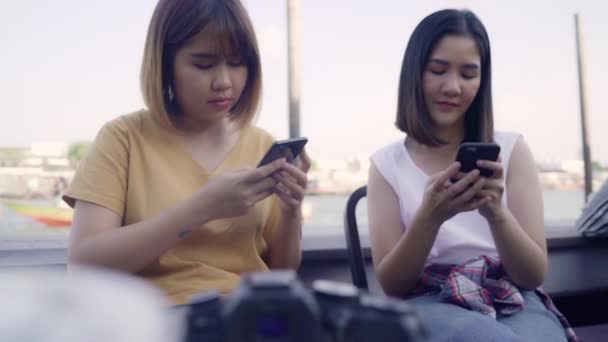 若いアジアの女性が近くの友人の観光客とカジュアルな楽しみとスマートフォンの共有写真でオンラインソーシャルメディアビューポート川の前のカフェ街で ライフスタイル観光旅行休日のコンセプト — ストック動画