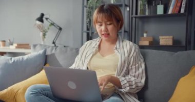 Serbest Asyalı kadın evdeki oturma odasında dizüstü bilgisayar kullanarak günlük kıyafet giyiyor. Evden çalışmak, uzaktan çalışmak, uzaktan eğitim, sosyal uzaklık, korona virüsünün önlenmesi için karantina.