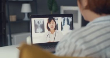 Bilgisayarlı dizüstü bilgisayar kullanan genç Asyalı kız video konferans görüşmesinde evdeki oturma odasında uzman doktorla hastalıktan bahsediyor. Coronavirus konsepti için sosyal uzaklık, karantina.