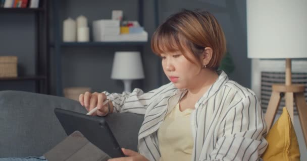 自由亚洲女士休闲装使用平板电脑在线学习在客厅的家 在家工作 远程工作 远程教育 社会疏离 为预防电晕病毒进行检疫 — 图库视频影像