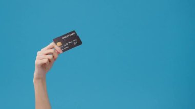 Genç kız, elinde kredi kartıyla stüdyoda mavi arka planda baş parmağının gözüktüğünü gösteriyor. Yer için bir metin, reklam için bir mesaj kopyala. Reklam alanı, promosyon içeriği.