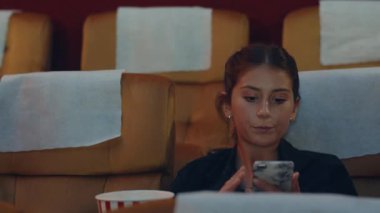 Çekici, neşeli, beyaz bir çift sinemada film izlerken akıllı telefon kullanıyor. Yaşam tarzı eğlence konsepti.