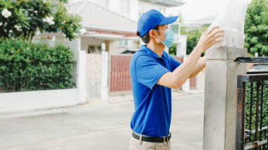 Genç postacı yüz maskesi takıyor ve evdeki müşterilere gönderilmek üzere yemek kutusuna bakıyor. Ve Asyalı kadın dışarıda paket alıyor. Corona virüsü kavramından sonra yaşam tarzı yeni normal.