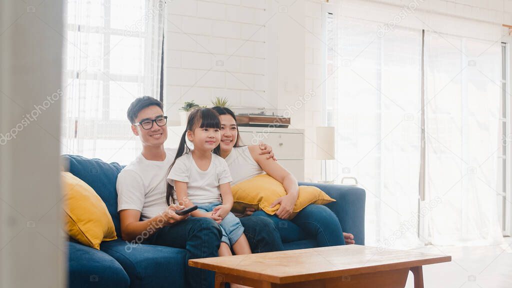 Happy Asian family enjoy their free time relax together at home. Lifestyle Korean dad, mom and daughter watching TV together and having fun lying on sofa in living room in modern house.