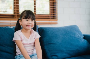 Mutlu Asyalı kız evde birlikte boş vakit geçirmenin keyfini çıkarıyor. Birlikte televizyon seyreden Koreli kadın çocuk. Modern evdeki oturma odasında kanepede uzanıp eğleniyor..