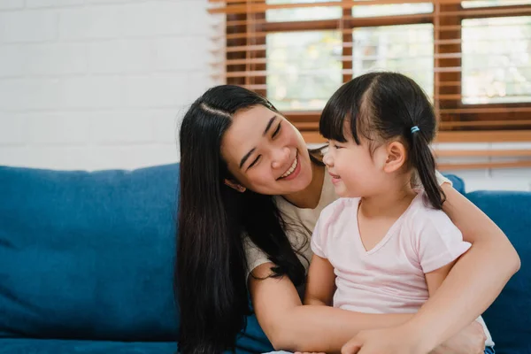 Happy Asian family mom and daughter embracing kissing on cheek congratulating with birthday at house. Self-isolation, stay at home, social distancing, quarantine for coronavirus prevention.