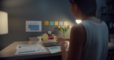 Genç Asyalı iş kadını serbest bilgisayar uzmanı ev gecesinde oturma odasındaki ahşap masa üzerinde çalışmaya başlamak için hazırlanıyor. Evden çalış, uzaktan, koronavirüs için karantina.