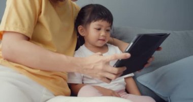 Mutlu mutlu Asya ailesi annesi ve sevimli çocuk dijital tablet ile ilgili çizgi film kullanıyor ve evdeki oturma odasındaki kanepede rahatça eğleniyor. Coronavirus karantinasında birlikte vakit geçiriyoruz..