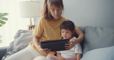 Mutlu mutlu Asya ailesi annesi ve sevimli çocuk dijital tablet ile ilgili çizgi film kullanıyor ve evdeki oturma odasındaki kanepede rahatça eğleniyor. Coronavirus karantinasında birlikte vakit geçiriyoruz..