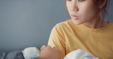 Mutlu, neşeli, Asya 'lı anne hasta bir bebeği kollarına alıp antipiretik jel yapıştırıyor ve evdeki oturma odasında bebek alnından öpüyor. Sağlık sigortası, tedavi ve sağlık hizmeti kavramı.