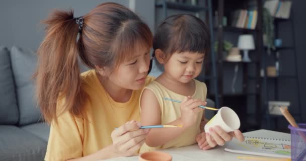 快乐快乐的亚洲家庭妈妈教蹒跚学步的小女孩画瓷壶在客厅的桌上玩乐放松 在一起度过的时间 社会距离 检疫以预防结肠炎 — 图库视频影像