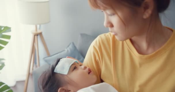 幸せな陽気なアジアの家族のお母さんは 病気の幼児の女の子を腕の中で保持し 家のリビングルームで赤ちゃんの額の散歩に解熱ジェルを添付します 医療保険 医療の概念 — ストック動画