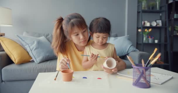 快乐快乐的亚洲家庭妈妈教蹒跚学步的小女孩画瓷壶在客厅的桌上玩乐放松 在一起度过的时间 社会距离 检疫以预防结肠炎 — 图库视频影像