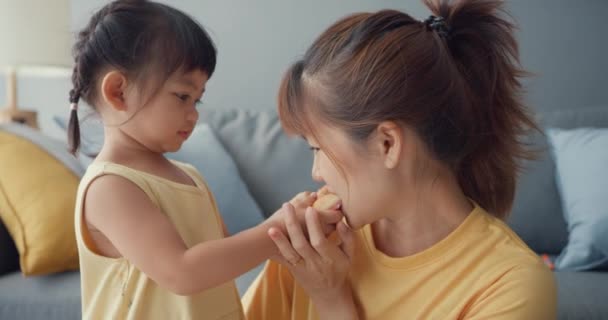幸せな陽気なアジアの家族のお母さんと幼児の女の子はドーナツを食べ 家のリビングルームでソファでリラックスしてお楽しみください 一緒に過ごす時間 社会的距離 コロナウイルスの隔離 — ストック動画