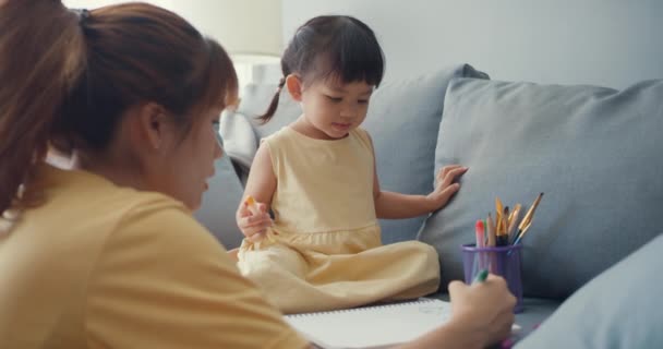 快乐快乐的亚洲家庭妈妈教女孩用相册和彩色铅笔在客厅的沙发上玩乐放松 在一起的时间 社会距离 — 图库视频影像