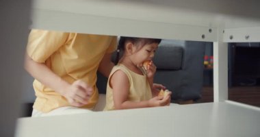 Mutlu mutlu Asya ailesi anne ve küçük kız donut yiyor ve evdeki kanepede keyfine bakıyor. Birlikte zaman geçirmek, sosyal uzaklık, koronavirüs karantinası..