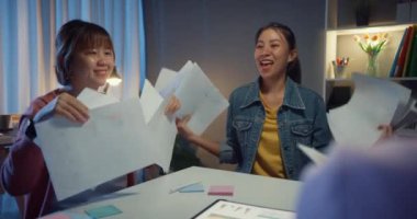 Çok ırklı bir grup genç Asyalı yaratıcı insanlar iş tartışırken giyiniyorlar proje başarısını kutluyorlar ve belge atıyorlar, gülüyorlar ve beyin fırtınası sırasında birlikte gülüyorlar..