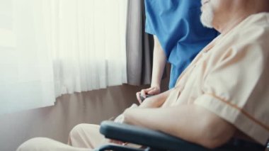 Genç Asyalı bakıcı kadın desteği, yaşlı adamın evde ya da hastanede tekerlekli sandalyeye oturmasına yardımcı oluyor. Rehabilitasyon aktivitesi, yaşlı sağlık hizmetleri tanıtımı, sağlık ve tıp konsepti.