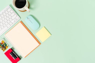 Çalışma masasının yaratıcı düz yatay fotoğrafı. Klavyesi, faresi ve pastel yeşil arka planda açık siyah defteri olan üst görünüm ofis masası. Üst görünüm, fotokopi alanı fotoğrafçılığıyla aynı..