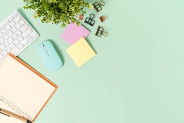 Çalışma masasının yaratıcı düz yatay fotoğrafı. Klavyesi, faresi ve pastel yeşil arka planda açık siyah defteri olan üst görünüm ofis masası. Üst görünüm, fotokopi alanı fotoğrafçılığıyla aynı..