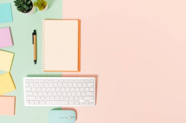 Çalışma masasının yaratıcı düz yatay fotoğrafı. Üzerinde klavye, fare ve açık maket siyah defter olan en iyi ofis masası. Pastel yeşil pembe arka planda. Üst görünüm, fotokopi alanı fotoğrafçılığıyla aynı..