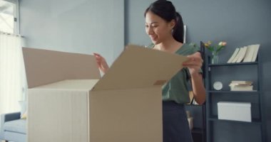 Mutlu Asya 'lı güzel bayan evdeki oturma odasındaki çevrimiçi pazardan karton teslimat paketini açıyor. İnternet üzerinden alışveriş yapan, boks yapmayan, online alışveriş ve dağıtım konsepti olan.