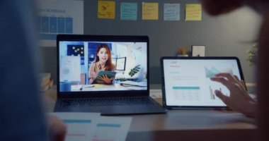 Genç Asya finans öğrencisi bayanlar online ders izliyor ve geceleri evden oturma odasında dizüstü bilgisayar ve tabletle ders çalışıyorlar. Bilgisayar ekranına bakarken not almak, çevrimiçi kavram öğrenmek.