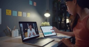 Dizüstü bilgisayar kullanan Asyalı kadın, masa başında iş arkadaşlarıyla oturma odasında çalışırken video görüşmeleri hakkında konuşurken grafiği görüyor. Kişisel izolasyon, sosyal uzaklık, koronavirüs için karantina.