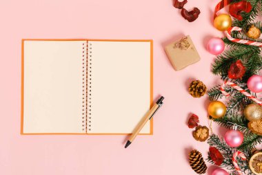 Kış, geleneksel Noel kompozisyonu ve yeni yıl tatili sezonunun en az yaratıcı düzlüğü. Üst görünüm, pembe arkaplandaki metin için siyah defter. Model yap ve uzay fotoğrafçılığını kopyala.