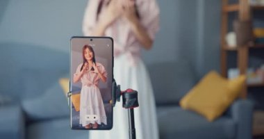 Happy young Asian girl blogger front of phone camera record video enjoy with dance content in living room at home. Social distance coronavirus pandemic concept. Freedom and active lifestyle concept