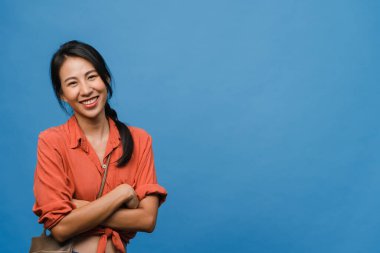 Olumlu ifadeli, kollarını kavuşturmuş, geniş bir şekilde gülümseyen, günlük kıyafetler giymiş ve mavi arka planda kameraya bakan genç Asyalı kadının portresi. Mutlu, mutlu, mutlu kadın başarıya sevinir..