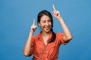 Neşeli bir ifadeyle gülümseyen Asyalı genç bir kadının portresi, boş bir alanda, günlük kıyafetlerle inanılmaz bir şey gösteriyor ve mavi arka planda izole edilmiş kameraya bakıyor. Yüz ifadesi kavramı.