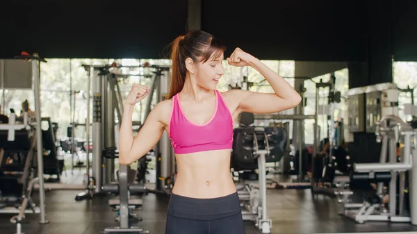 Happy Asian healthy sport woman trainer with sportswear smiling looking at camera show arms muscle after workout in gym, People Training use in fitness class, sport and healthy lifestyle concept.
