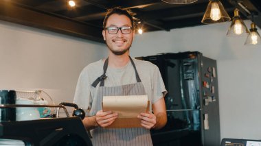 Genç Asyalı baristanın portresi şehir kafesinde kendini mutlu hissederek menüden sipariş alıyor. Asya 'daki küçük işletme sahibi çocuk rahatla dişlek gülümseme kahve dükkanında kameraya bakıyor..