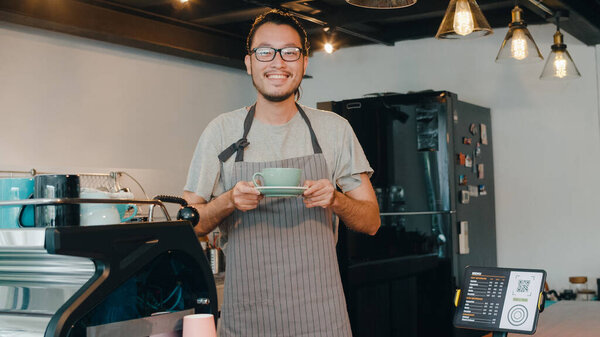 Portrait young Asian guy barista waitress holding coffee cup feeling happy at urban cafe. Asia small business owner boy in apron relax toothy smile looking to camera stand at counter in coffee shop.