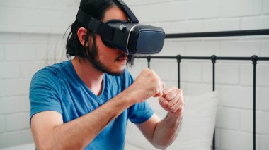 Genç Asyalı adam gözlük kullanarak sanal gerçeklik simülatörü kullanıyor. Yatak odasında boks oynuyor. Japon erkek kendini mutlu hissediyor. Gençler oyun oynuyor. Ev konseptinde rahatlayın..