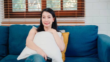 Genç Asyalı kadın evde televizyon seyrediyor, kadın oturma odasında kanepede uzanmış kendini mutlu hissediyor. Yaşam tarzı kadını sabah konseptinde rahatlar..