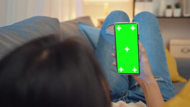 年轻的亚洲女士在现代家庭夜晚坐在客厅的沙发上休息时 使用带有空白绿色屏幕的智能手机进行广告文字的模拟展示 色谱关键技术 营销设计理念 — 图库视频影像