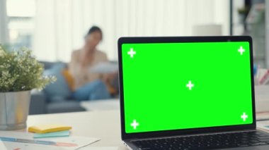 Boş yeşil ekranlı bilgisayar laptopu modern evdeki oturma odasındaki masada duran reklam metinlerini taklit ediyor. Chroma anahtar teknolojisi, pazarlama tasarım konsepti.