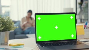 Boş yeşil ekranlı bilgisayar laptopu modern evdeki oturma odasındaki masada duran reklam metinlerini taklit ediyor. Chroma anahtar teknolojisi, pazarlama tasarım konsepti.
