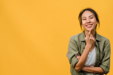 Olumlu ifadeli, kollarını kavuşturmuş, geniş bir şekilde gülümseyen, sıradan kıyafetler giymiş ve sarı arka planda kameraya bakan genç Asyalı kadının portresi. Mutlu, mutlu, mutlu kadın başarıya sevinir..