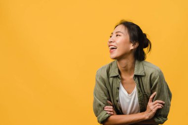 Asyalı genç bir kadının portresi, olumlu bir ifade, kolları çapraz, geniş bir gülümseme, sarı arka planda gündelik giysiler içinde. Mutlu, sevimli, mutlu kadın başarıya sevinir. Yüz ifadesi kavramı.