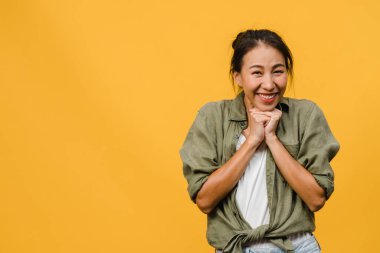 Olumlu ifadeli genç Asyalı bayan, geniş bir gülümseme, günlük kıyafetler giymiş ve sarı arka plandan kameraya bakıyor. Mutlu, sevimli, mutlu kadın başarıya sevinir. Yüz ifadesi kavramı.