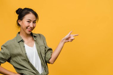 Neşeli bir ifadeyle gülümseyen Asyalı genç bir kadının portresi boş bir alanda, sarı arka planda izole edilmiş bir kameraya bakarak inanılmaz bir şey gösteriyor. Yüz ifadesi kavramı.