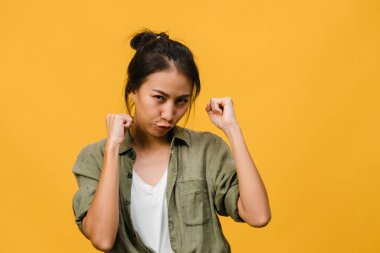 Olumlu ifadeli, neşeli ve heyecan verici, günlük giysiler içinde genç bir Asyalı kadın ve sarı arka plandaki kameraya bakın. Mutlu, sevimli, mutlu kadın başarıya sevinir. Yüz ifadesi kavramı.