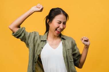 Olumlu ifadeli, neşeli ve heyecan verici, sarı arka planda boş alan olan günlük giysiler giymiş genç Asyalı bayan. Mutlu, sevimli, mutlu kadın başarıya sevinir. Yüz ifadesi kavramı.