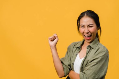Olumlu ifadeli, neşeli ve heyecan verici, günlük giysiler içinde genç bir Asyalı kadın ve sarı arka plandaki kameraya bakın. Mutlu, sevimli, mutlu kadın başarıya sevinir. Yüz ifadesi kavramı.