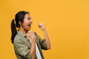 Olumlu ifadeli, neşeli ve heyecan verici, sarı arka planda boş alan olan günlük giysiler giymiş genç Asyalı bayan. Mutlu, sevimli, mutlu kadın başarıya sevinir. Yüz ifadesi kavramı.